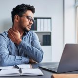 a man sits in the office with a painful strain in his neck